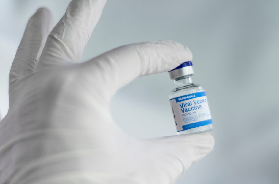 Hand wearing a surgical glove holding a small bottle of the SARS-CoV-2 Viral Vector Vaccine.
