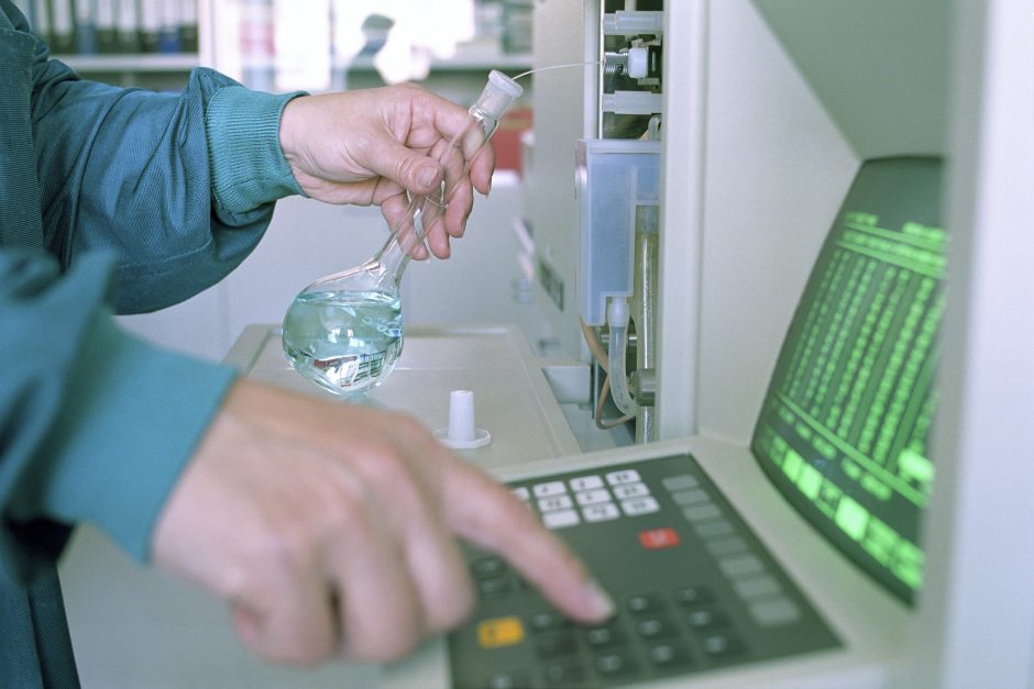 In a lab, a person holds a beaker with a clear fluid inside while typing into a computer console.