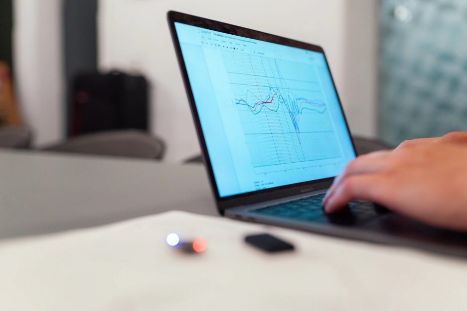 An image of a person typing on a laptop. The laptop screen shows a graph with blue, red, and green lines.